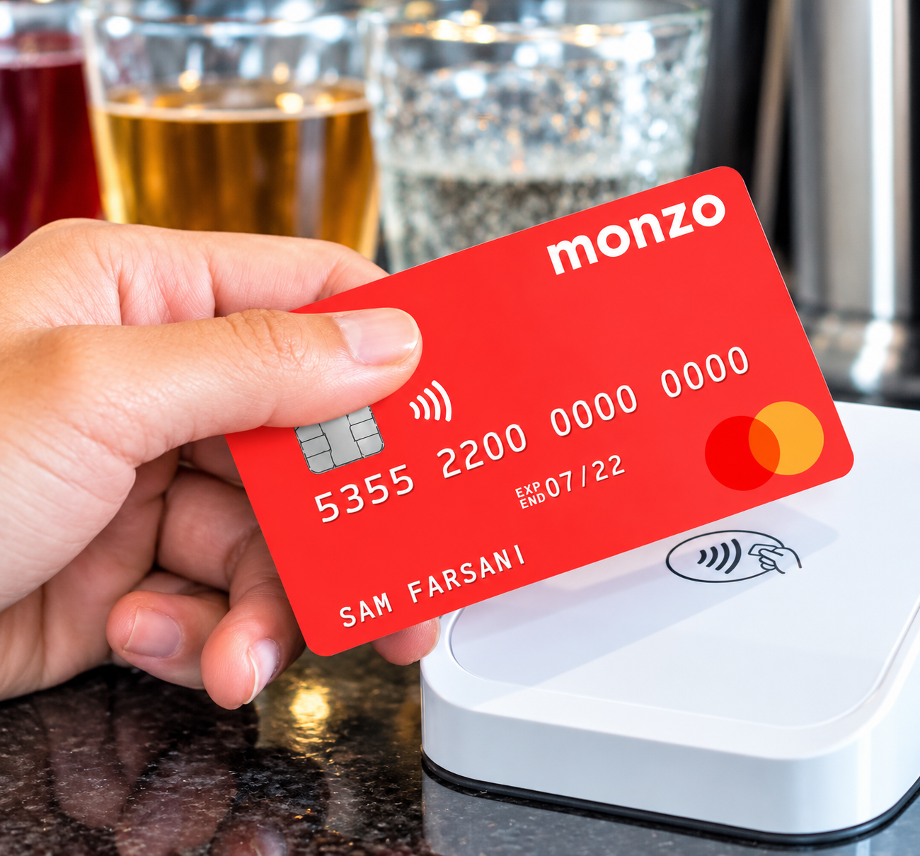 Main tenant une carte MONZO rouge au-dessus d’un terminal de paiement sans contact